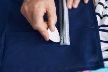 Orta yaşlı, gri saçlı bir adam terzi dükkanında kumaşa iz bırakmış.