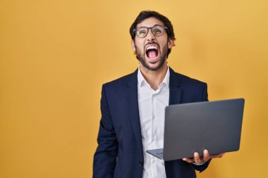 Bilgisayar dizüstü bilgisayar kullanan yakışıklı Latin adam sinirli ve kızgın bağırıyor ve öfkeden köpürüyor. Öfkeyle bağırıyor. öfke ve agresif konsept. 