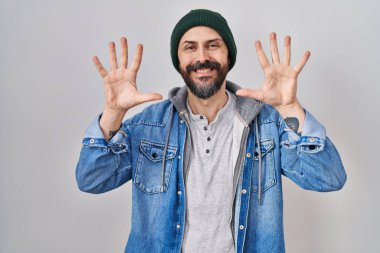 Dövmeli, yün şapkalı, on numaralı parmaklarıyla onu gösteren, kendinden emin ve mutlu gülümseyen İspanyol genç adam.. 