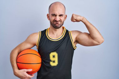 Basketbol forması giyen, sakallı, genç, kel bir adam. Elinde top tutan güçlü, kol kaslı, kendinden emin ve gururlu biri. 