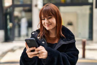 Sokakta akıllı telefon kullanan kendine güvenen genç bir kadın.