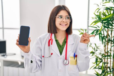 Genç İspanyol doktor kadın akıllı telefon ekranı gösteriyor. Parmağını yana doğru gösteriyor. Gülümsüyor, ağzı açık. 