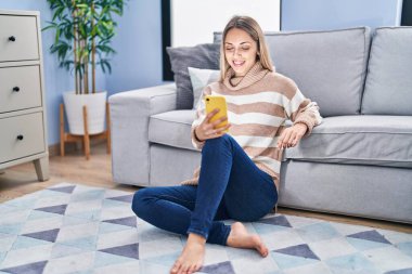 Young woman using smartphone sitting on floor at home