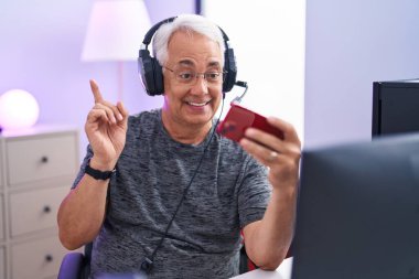 Gri saçlı orta yaşlı bir adam akıllı telefonuyla video oyunu oynuyor. Gülümsüyor, mutlu bir şekilde elini ve parmağını yana uzatıyordu. 