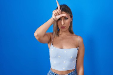 Mavi arka planda dikilen genç bir kadın alnında parmakları olan insanlarla dalga geçiyor. Ezik hareketler yapıyor, alay ediyor ve hakaret ediyor.. 