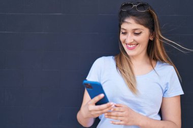Young hispanic woman smiling confident using smartphone over black background