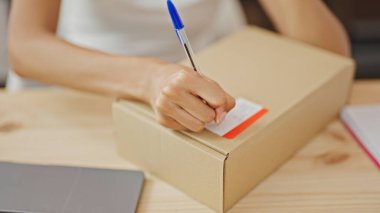 Afrika kökenli Amerikalı kadın ecommerce işçisi ofiste paket üzerine yazıyor.