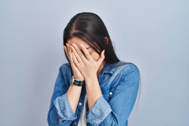 Mavi arka planda dikilen İspanyol kadın. Ağlarken yüzünü ellerle kapatan üzgün bir ifade. depresyon kavramı. 