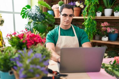 Young hispanic man florist using laptop at flower shop