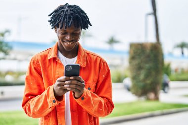 Sokakta akıllı telefon kullanan, kendinden emin gülümseyen Afrikalı Amerikalı bir adam.