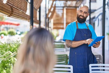 Young bald man waiter smiling confident using touchpad at coffee shop terrace