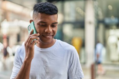 Genç Latin adam gülümsüyor. Kendine güveniyor. Akıllı telefondan konuşuyor.