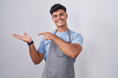 Beyaz arka planda önlük giyen İspanyol genç adam kameraya hayret ediyor ve gülümsüyor.. 