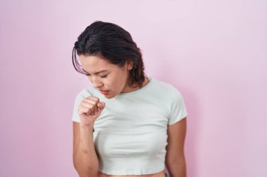 Pembe arka planda duran İspanyol genç kadın kendini kötü hissediyor ve soğuk algınlığı veya bronşitin belirtisi olarak öksürüyor. sağlık hizmeti kavramı. 