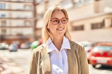 Genç sarışın kadın yönetici gülümseyerek caddede duruyor.