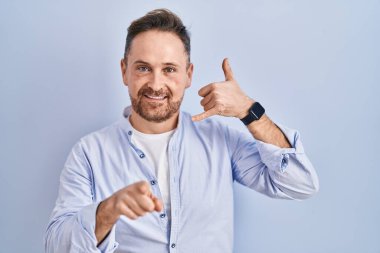 Orta yaşlı beyaz bir adam mavi arka planda durup gülümsüyor telefonda konuşuyor ve seni işaret ediyor. Ara beni.. 