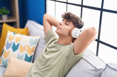 Genç İspanyol genç evdeki kanepede rahatça müzik dinliyor.