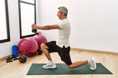 Spor merkezinde kettlebell eğitimi alan orta yaşlı gri saçlı bir adam.