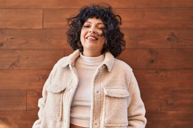 Young beautiful hispanic woman smiling confident standing over isolated wooden background
