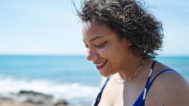 Genç, güzel, Latin bir kadın, gülümsüyor. Deniz kenarında kendine güveniyor.