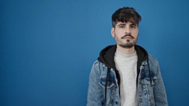 Soyutlanmış mavi arka planda ciddi bir ifadeyle duran İspanyol genç adam.