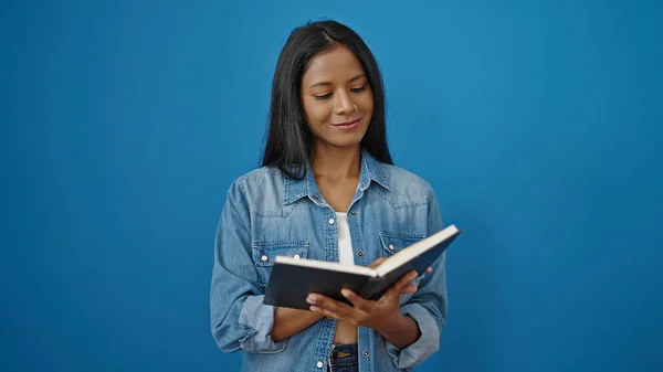 アフリカ系アメリカ人女性笑顔自信に満ちた読書本上の隔離された青の背景 — ストック写真