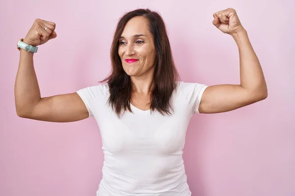 Middelbare Leeftijd Brunette Vrouw Staan Roze Achtergrond Tonen Armen Spieren — Stockfoto