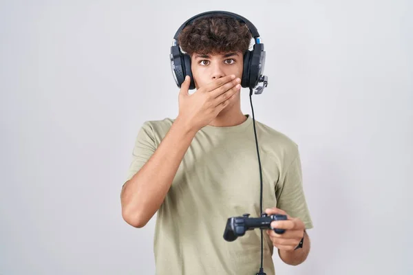 Hispanic Teenager Playing Video Game Holding Controller Shocked Covering Mouth — Stock Photo, Image