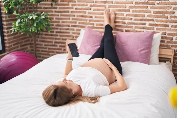 Mujer Embarazada Joven Usando Teléfono Inteligente Tocando Vientre Dormitorio — Foto de Stock
