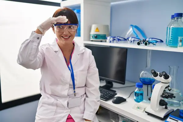 科学研究所で働いている若いブルネットの女性は 頭の上に手で遠くを見て非常に幸せと笑顔 検索の概念 — ストック写真