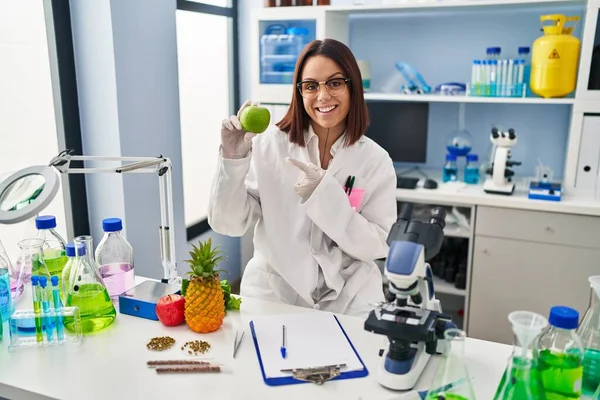 在科学家实验室工作的年轻惊慌失措的女人 手指手画脚地微笑着 喜形于色 — 图库照片