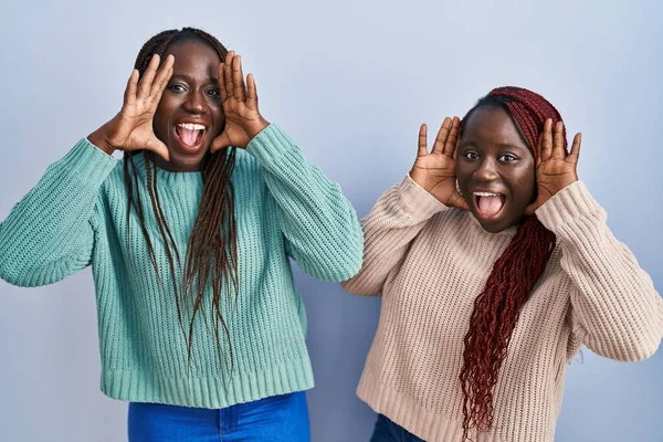 青い背景の上に立っている2人のアフリカ人女性が陽気に顔を見せる手で竹を覗き見て笑っている びっくりして興奮しました — ストック写真