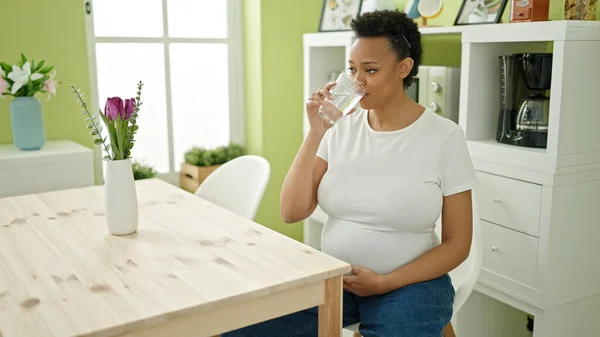 年轻的孕妇坐在饭厅的桌子上喝着一杯水 — 图库照片
