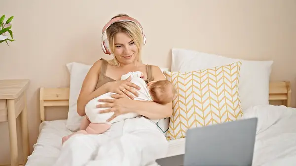 ベッドに座っている母と娘 授乳中の赤ちゃん 寝室で音楽を聴く — ストック写真