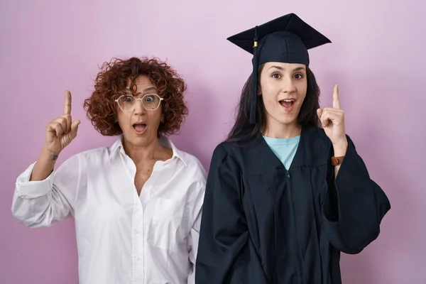 ヒスパニック系の母親と娘の卒業キャップと式のローブを着て成功したアイデアで指を指している 興奮して幸せよ 第1位 — ストック写真