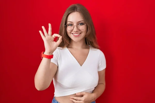 Młoda Kaukaska Kobieta Stojąca Nad Czerwonym Tłem Uśmiechnięta Pozytywnie Robiąca — Zdjęcie stockowe
