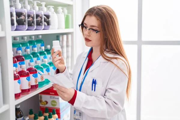 年轻的红头发女药剂师在药店拿着药瓶看药方 — 图库照片