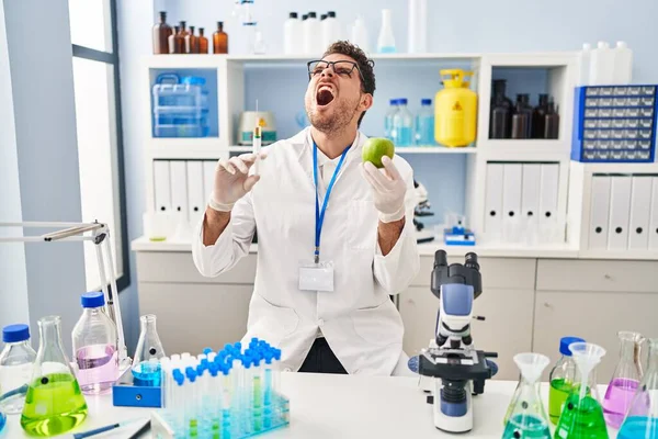 Young Hispanic Man Working Scientist Laboratory Holding Apple Angry Mad — Foto de Stock