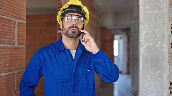 在建筑工地 他的年轻员工戴着安全帽 在智能手机上说话 — 图库照片