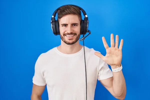 一个留着胡子的西班牙男人 一边戴着耳机听音乐 一边拿着五号手指指指指点点 自信而快乐地微笑着 — 图库照片