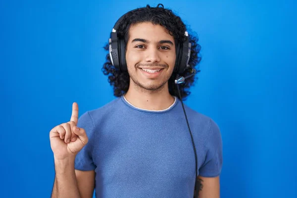 自信と幸せな笑顔ながら 第一指で示すと指差すヘッドフォンを使用して音楽を聞いて巻き毛のヒスパニック系の男 — ストック写真