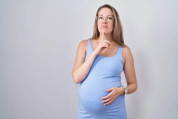 若いです妊娠中の女性立ちます上の白い背景思考濃縮の疑いについて指で顎と上を見上げ疑問 — ストック写真