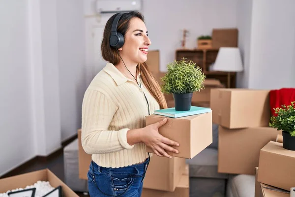 Young Beautiful Hispanic Woman Listening Music Holding Package New Home — Stockfoto