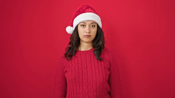 年轻而美丽的惊慌失措的女人站在那里 脸上带着严肃的表情 戴着圣诞帽 披着孤零零的红色背景 — 图库照片