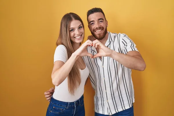 Sarı Arka Planda Dikilen Genç Çift Aşka Gülümsüyor Elleriyle Kalp — Stok fotoğraf