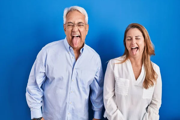 Medelålders Latinamerikanska Par Står Över Blå Bakgrund Sticker Tungan Glad — Stockfoto