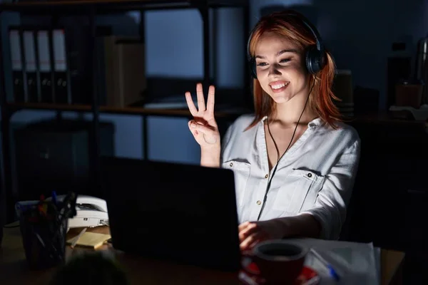 年轻的高加索女人晚上在办公室里工作时 带着自信和快乐的笑容 用手指指指第三号 — 图库照片