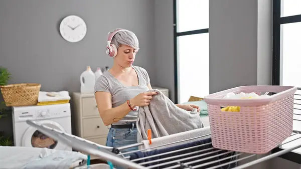 洗濯室で洋服を吊るす音楽を聴く若い女性 — ストック写真