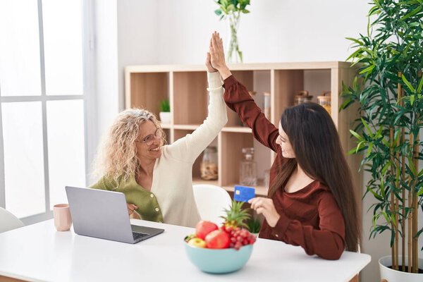 Две женщины мать и дочь используют ноутбук и кредитную карту дома