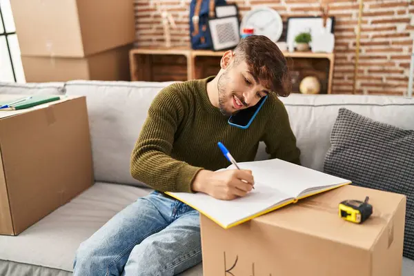 Jovem Árabe Homem Falando Smartphone Escrevendo Notebook Nova Casa — Fotografia de Stock